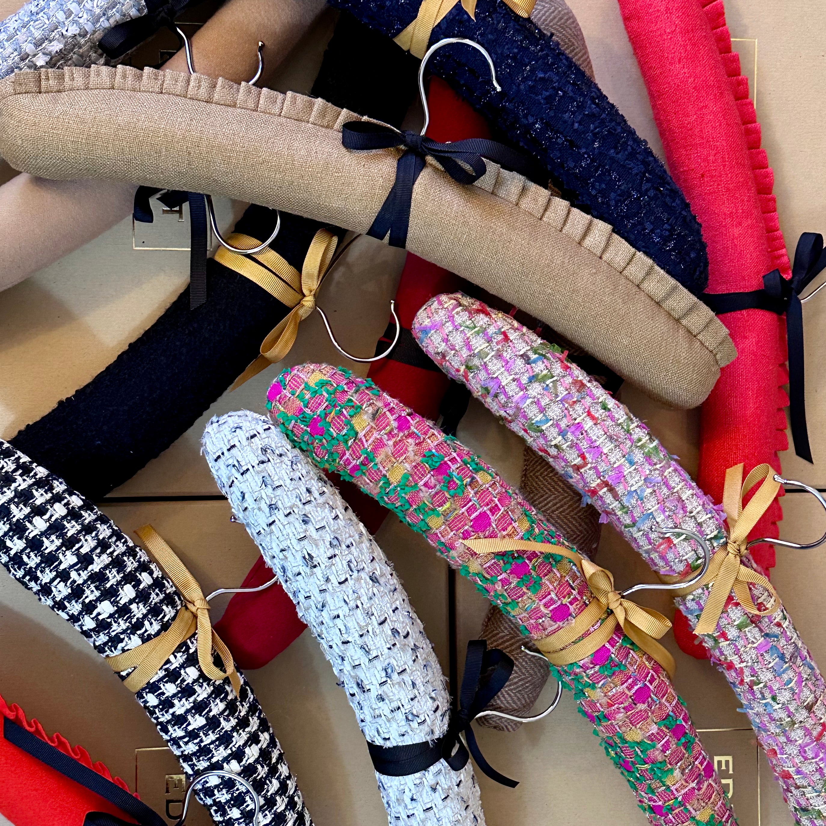A stack of textured, colourful hangers s, each tied with a gold ribbon. Hand made hangers, conjured from cut offs generated by EdNerat which makes on a zero waste basis. Made in Wales