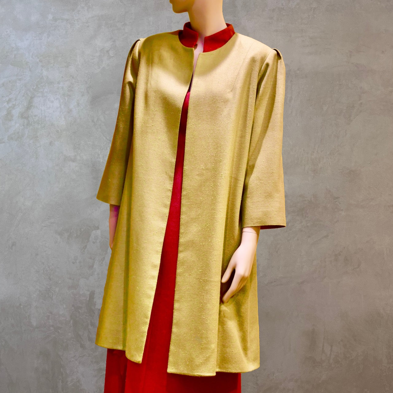 Full modelled view of Silk car coat in lime green. This is a Mid length coat with shoulder detail in an easy to wear trapeze shape. Fully lined in silk and made by hand in London. Worn over pink dress.