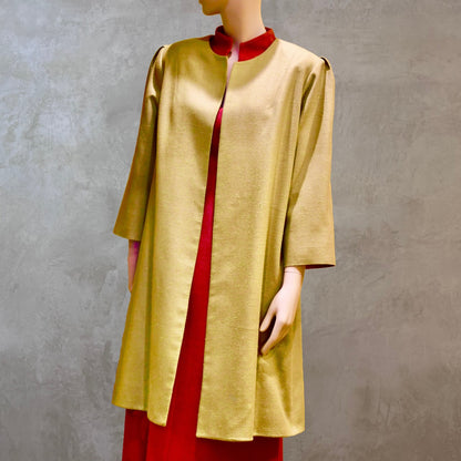 Full modelled view of Silk car coat in lime green. This is a Mid length coat with shoulder detail in an easy to wear trapeze shape. Fully lined in silk and made by hand in London. Worn over pink dress.