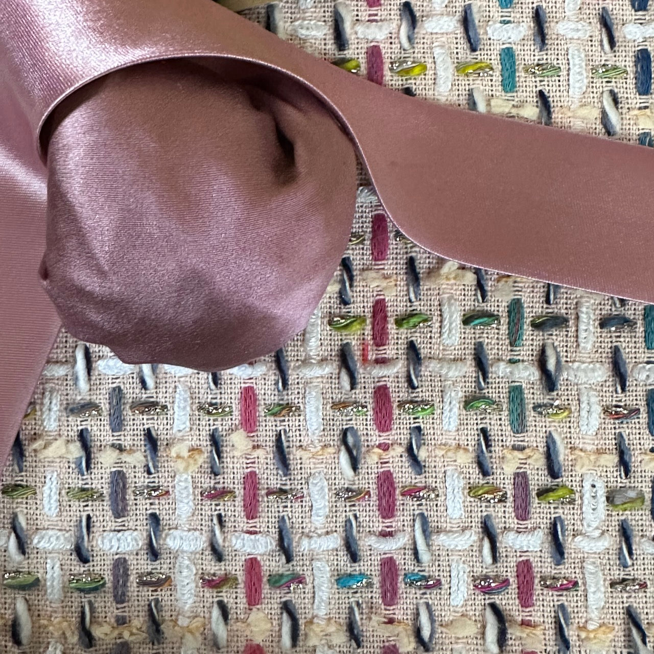 A close up of the Linton Tweeds fabric used in Ednerat's Boucle Bell Sleeve A-Line Coat, crafted from fabric adorned with vibrant stitches of red, blue, green, yellow, and white. Handmade in Britain.