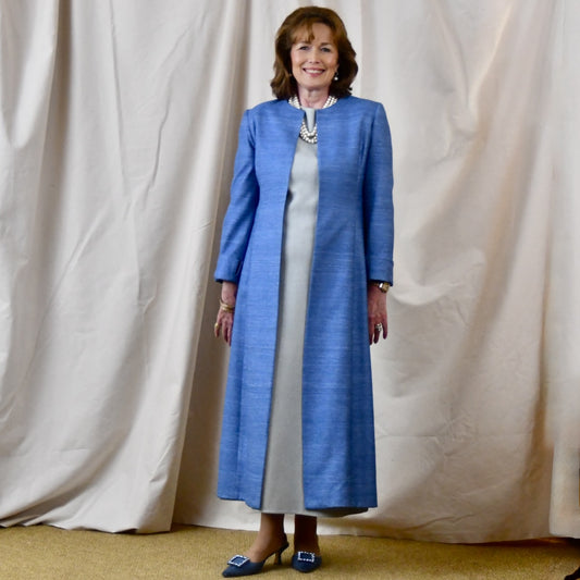 Tailored, Fitted Hourglass shaped coat in a summer-weight Silk Madras in Blue. This is a long-sleeved, calf-length blue summer coat with an hourglass shape. Shown from the side-front. A perfect summer coat for weddings and special occasions. Handmade in Britain.