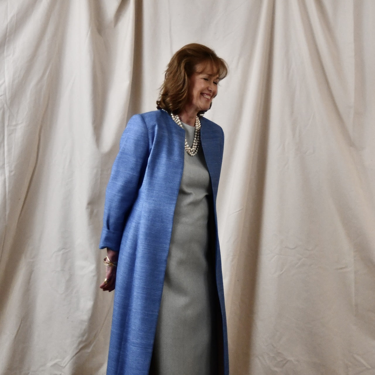 Tailored, Fitted Hourglass shaped coat in a summer-weight Silk Madras in Blue. This is a long-sleeved, calf-length blue summer coat with an hourglass shape. Shown from the side-front. A perfect summer coat for weddings and special occasions. Handmade in Britain.