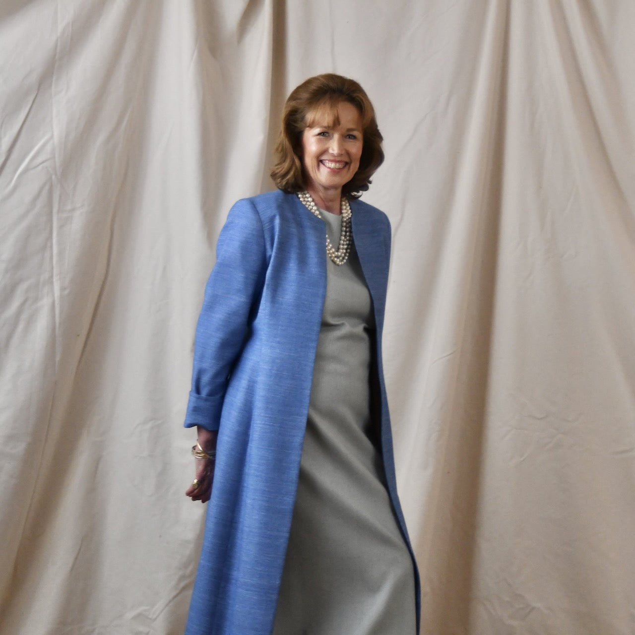 Tailored, Fitted Hourglass shaped coat in a summer-weight Silk Madras in Blue. This is a long-sleeved, calf-length blue summer coat with an hourglass shape. Shown from the side-front. A perfect summer coat for weddings and special occasions. Handmade in Britain.