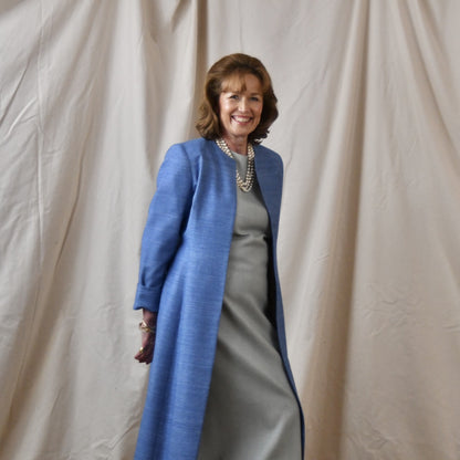 Tailored, Fitted Hourglass shaped coat in a summer-weight Silk Madras in Blue. This is a long-sleeved, calf-length blue summer coat with an hourglass shape. Shown from the side-front. A perfect summer coat for weddings and special occasions. Handmade in Britain.