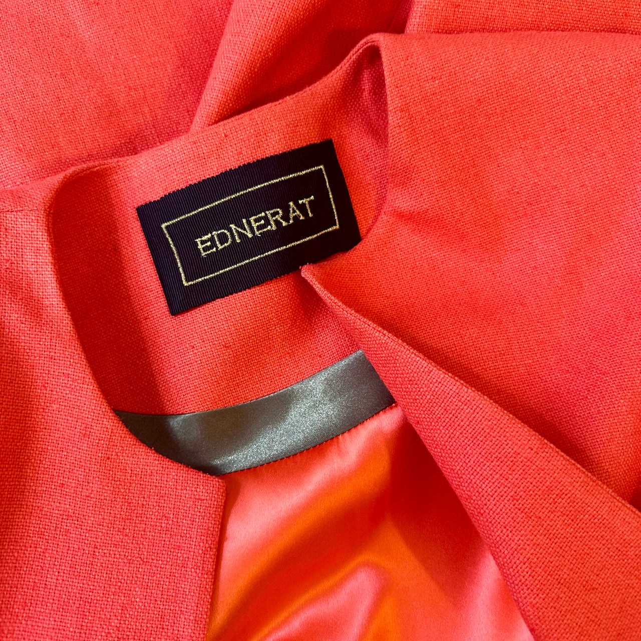 Tailored, Fitted, Hourglass Coat in Orange Silk Matka. Detail of this hourglass shaped coat showing the inside collar, and maker's label with gold lettering. The lustrous saffron silk lining adds a luxurious touch. Handmade in Britain.