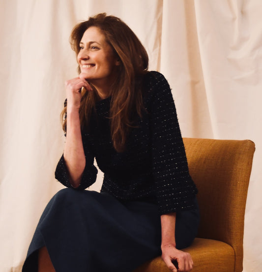 A woman with long brown hair, wearing a Tailored Boat Neck Blouse in Navy, Black and White Cotton Boucle and a navy skirt.
Handmade in Britain.