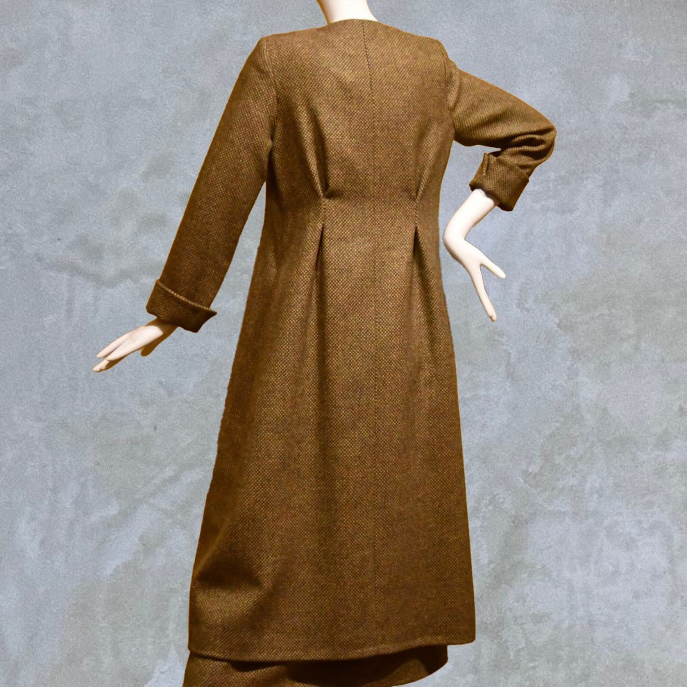 Longer length Skirted Hourglass Coat in Orange-Green Tweed. This shaped coat uses clever tailoring details to create a wonderfully flattering and easy to way skirted shape. With waist-enhancing tucks it will flatter the most testing of frames.  Entirely made in Great Britain. Back View, showing rear ruck detail.
