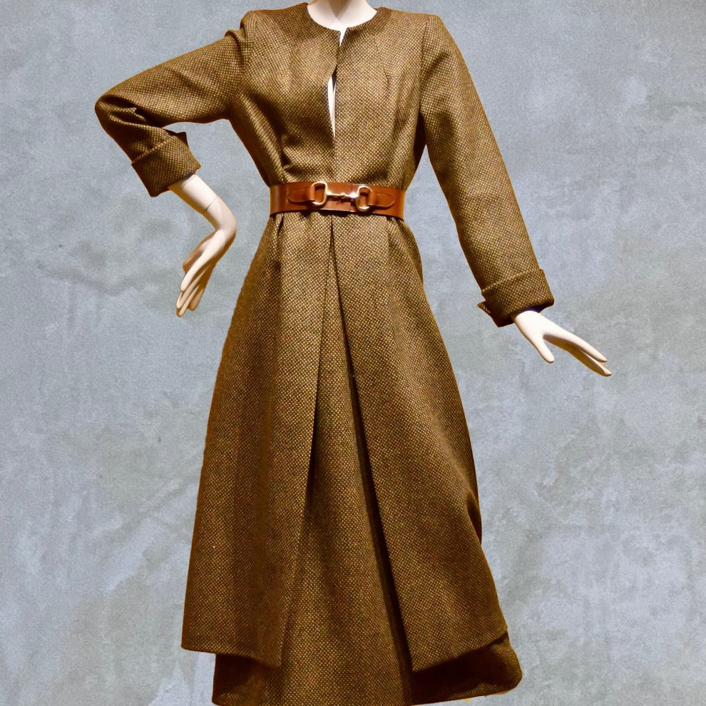 Longer length Skirted Hourglass Coat in Orange-Green Tweed. This shaped coat uses clever tailoring details to create a wonderfully flattering and easy to way skirted shape. With waist-enhancing tucks it will flatter the most testing of frames.  Entirely made in Great Britain. Worn closed with matching skirt, making sublime tweed skirt suit.