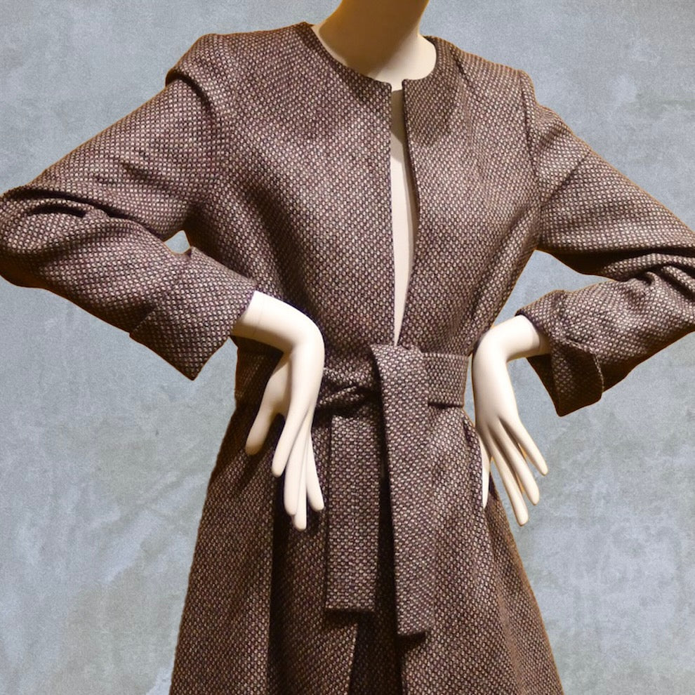 Long fitted tweed coat in pink colour. The ankle-length coat showcases a gray-pink textured tweed, hourglass tailoring, fitted seams, and back tucks. Handmade in Britain. Belted option close up.