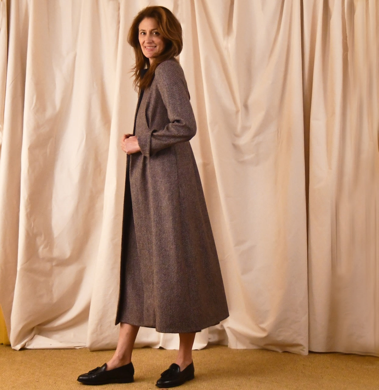 Long fitted tweed coat in pink colour. The ankle-length coat showcases a gray-pink textured tweed, hourglass tailoring, fitted seams, and back tucks. Handmade in Britain. Side View