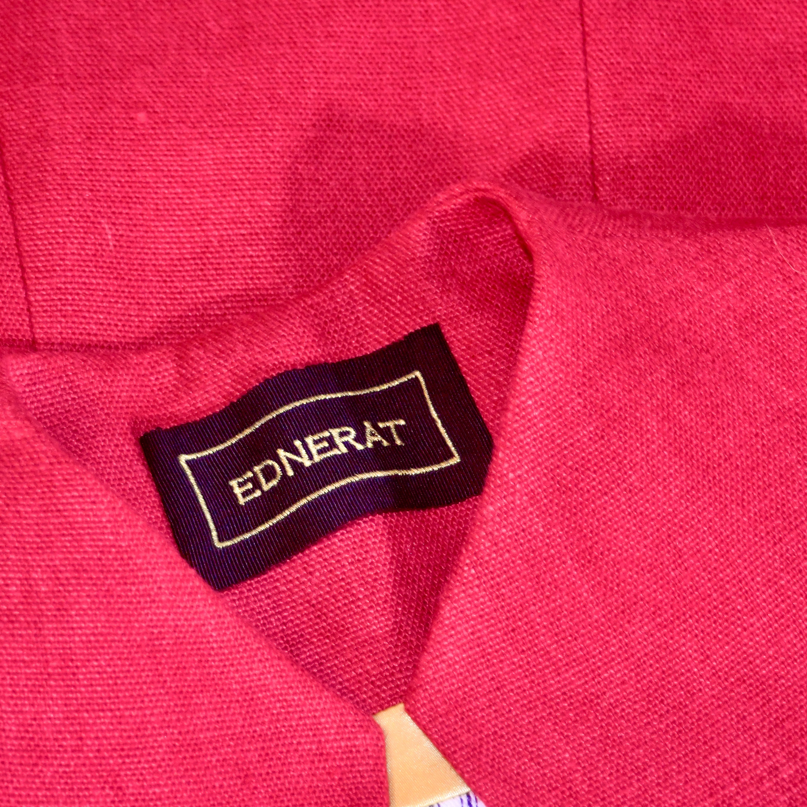A close-up of a red tailored fabric garment featuring a black clothing label that reads EDNERAT in white letters.