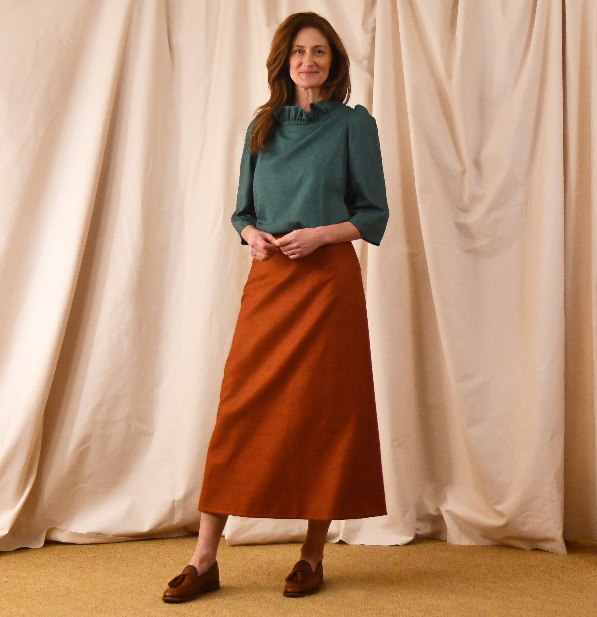 The Simple A-Line Skirt in Burnt Brick Silk Matka, paired with an emerald green frill top with three quarter length sleeves. Handmade in Britain.
