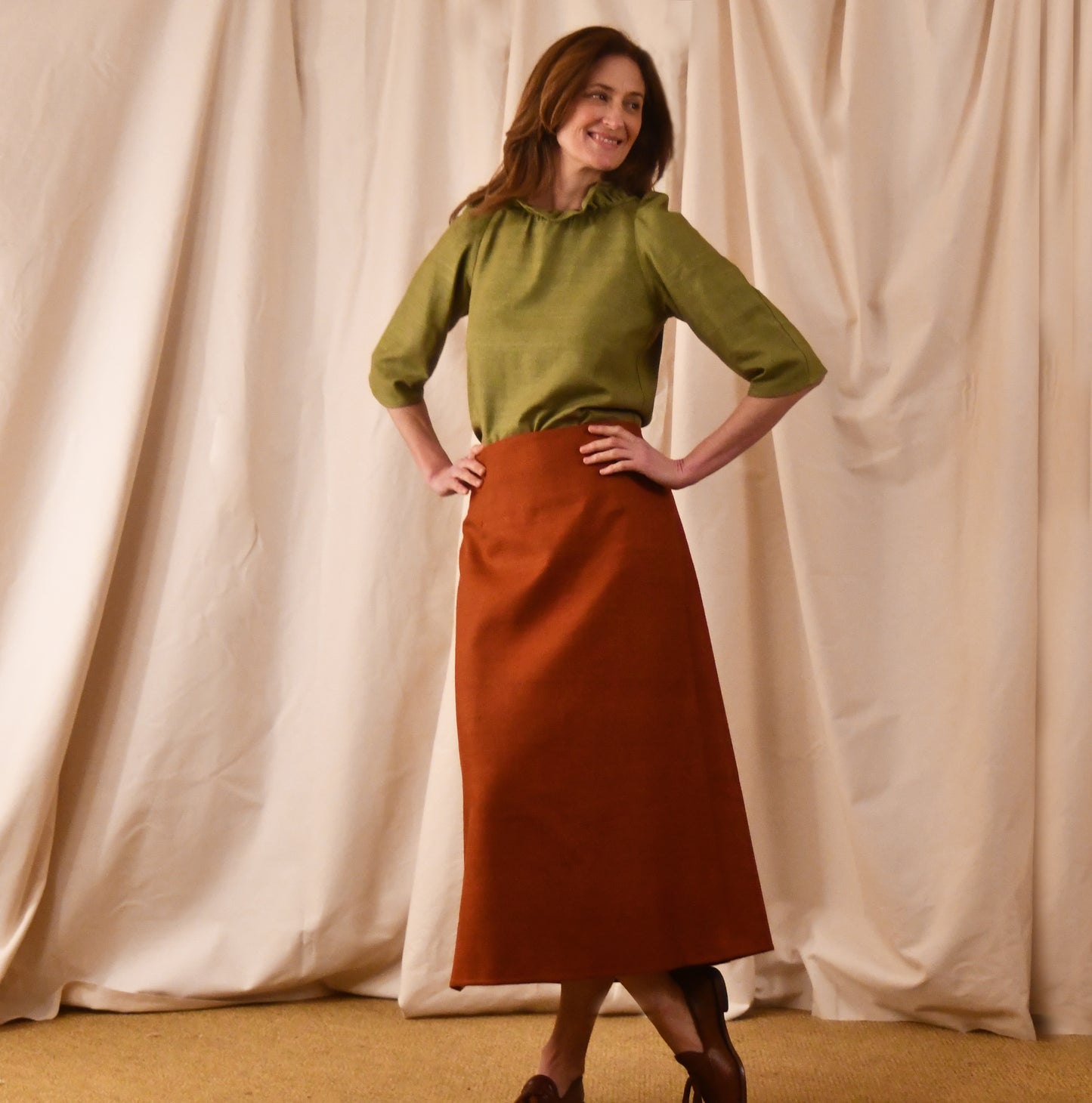 A Simple A-Line Skirt in Burnt Brick Silk Matka, paired with a light green tulip-sleeve blouse and brown loafers. an elegant and light summer outfit. Handmade in Britain.