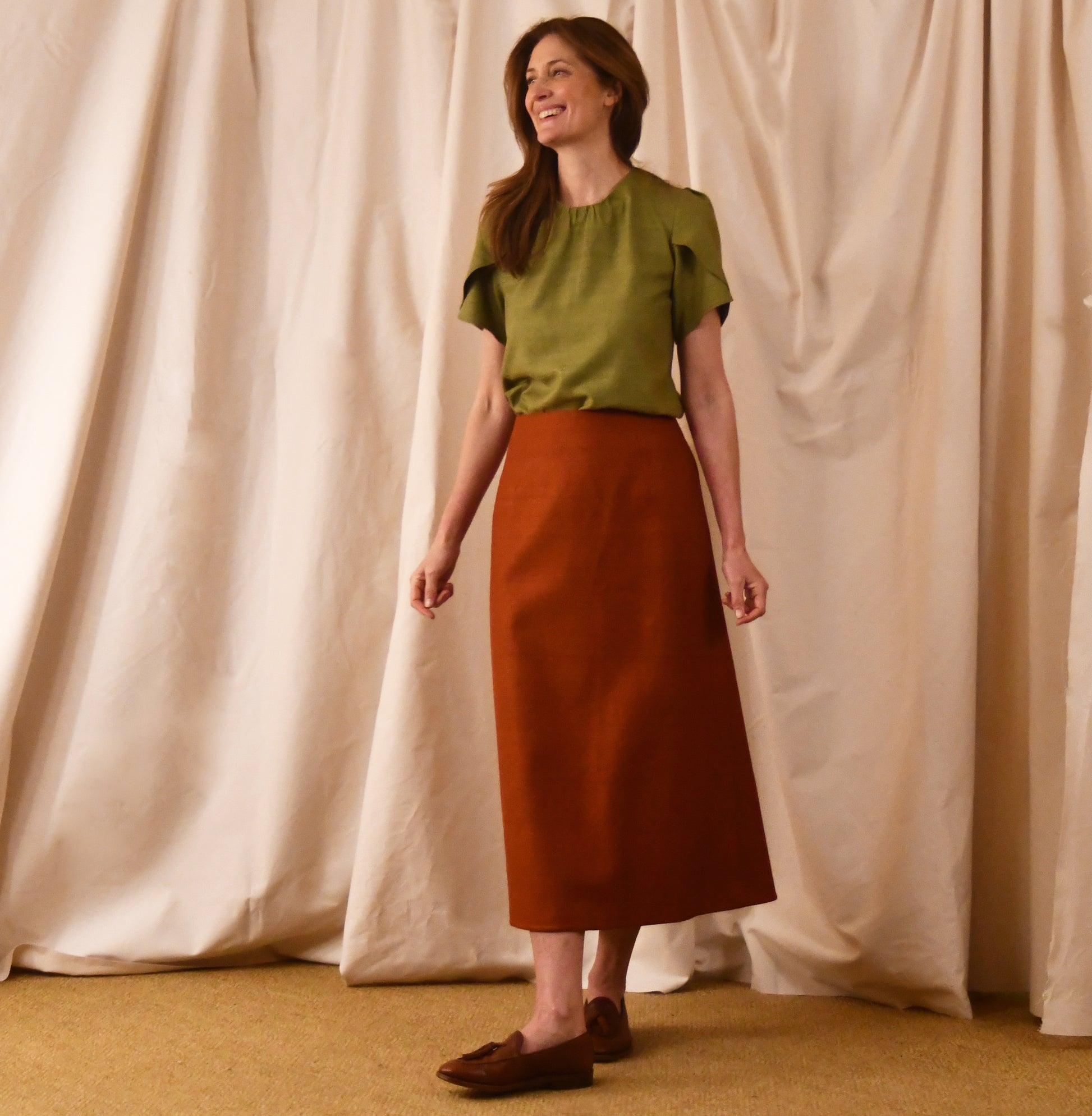 A Simple A-Line Skirt in Burnt Brick Silk Matka, paired with a light green tulip-sleeve blouse and brown loafers. an elegant and light summer outfit. Handmade in Britain.