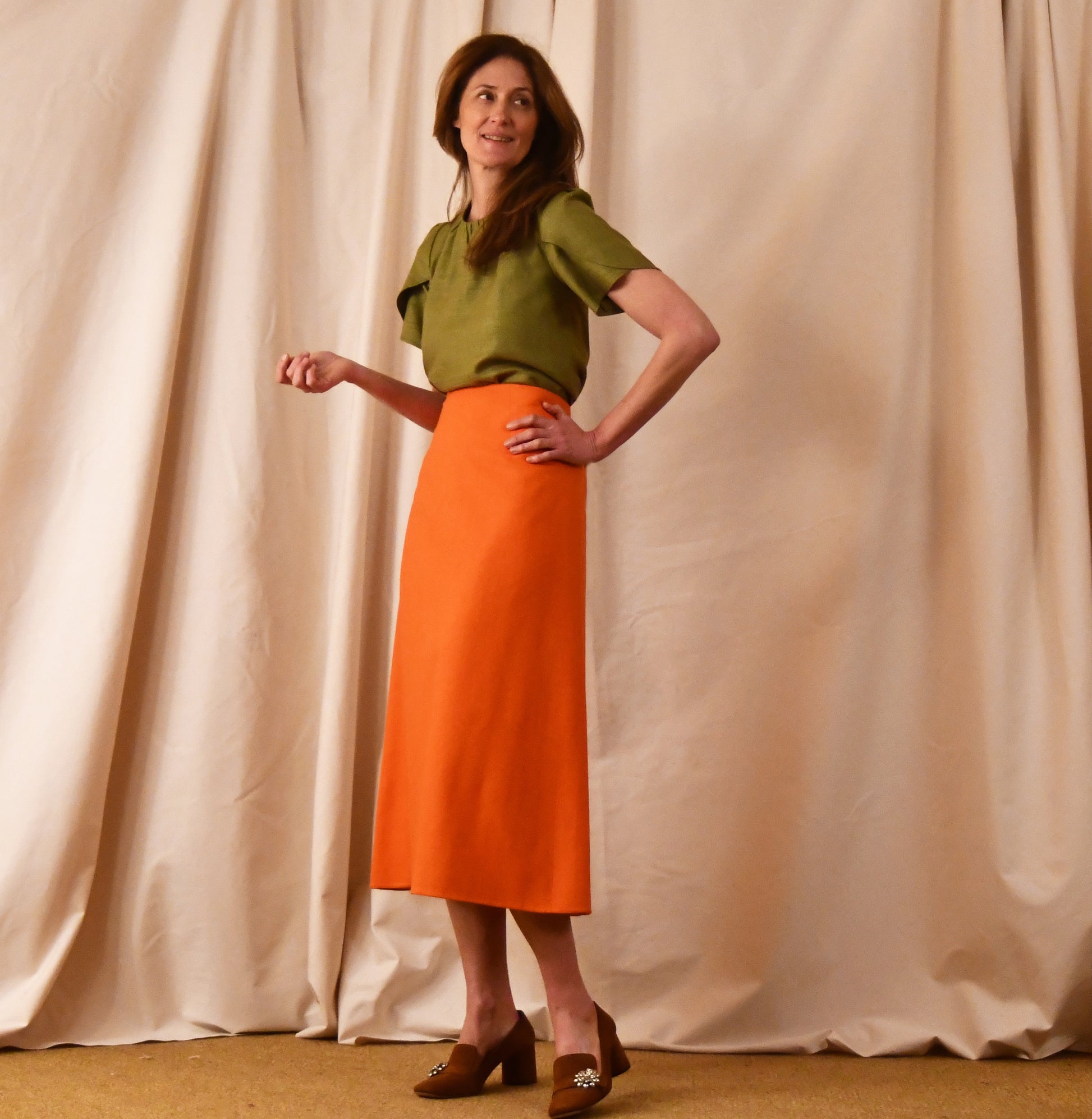 A Simple A-Line Skirt in Orange Silk Matka, paired with a light green tulip-sleeve blouse and brown loafers. an elegant and light summer outfit. Handmade in Britain.
