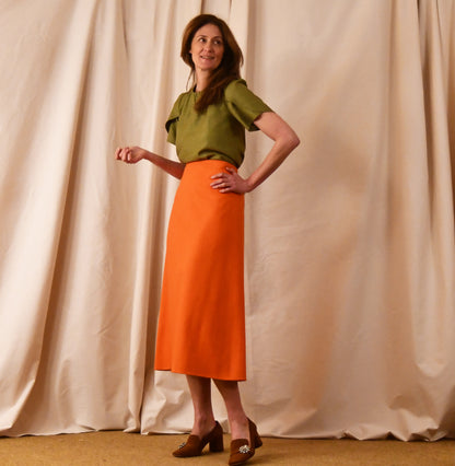 A Simple A-Line Skirt in Orange Silk Matka, paired with a light green tulip-sleeve blouse and brown loafers. an elegant and light summer outfit. Handmade in Britain.