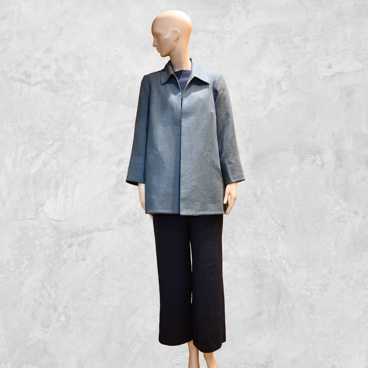 Light Blue Swing Jacket in Irish Linen. Easy and elegant jacket with cuff detail, slant pockets and a wide neck. Handmade in Britain. Full View over Navy Linen Trousers.