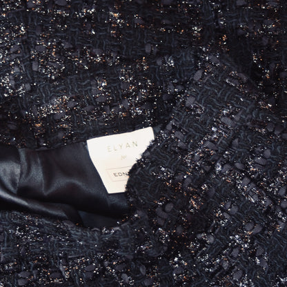 Close-up of the textured, dark, sparkly bouclé fabric from EdNerat’s The Waisted A-Line Skirt in Boucle. The smooth black lining contrasts with the textured outer material. Visible clothing label reads ELYAN for EDNA.