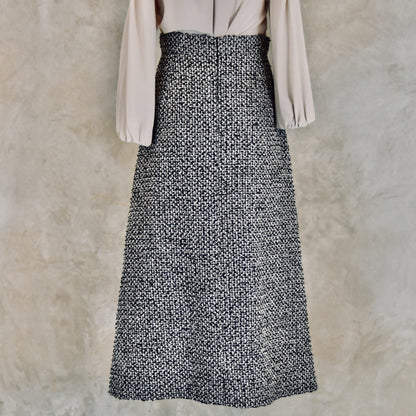The EdNerat Waisted A-Line Skirt in Linton Tweeds Bouclé with a light-colored, long-sleeve blouse. Handmade in Britain.