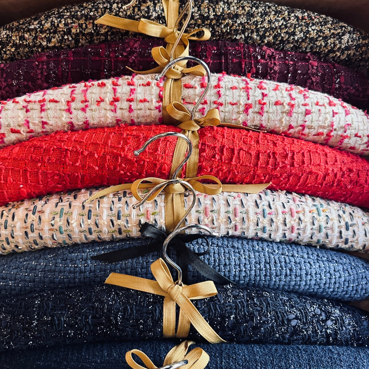 A stack of textured, colourful hangers s, each tied with a gold ribbon. Hand made hangers, conjured from Linton Tweeds cuf offs generated by EdNerat which makes on a zero waste basis. Made in Wales