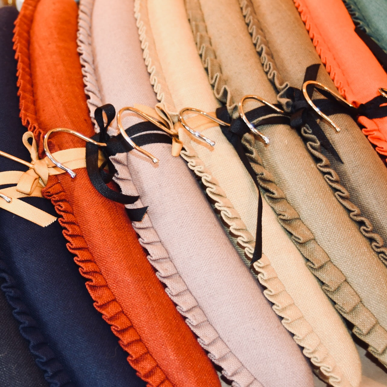 A stack of textured, colourful hangers, each tied with a gold ribbon. Hand made hangers, conjured from cut offs generated by EdNerat which makes on a zero waste basis. Made in Wales, Made from Pure Silk.