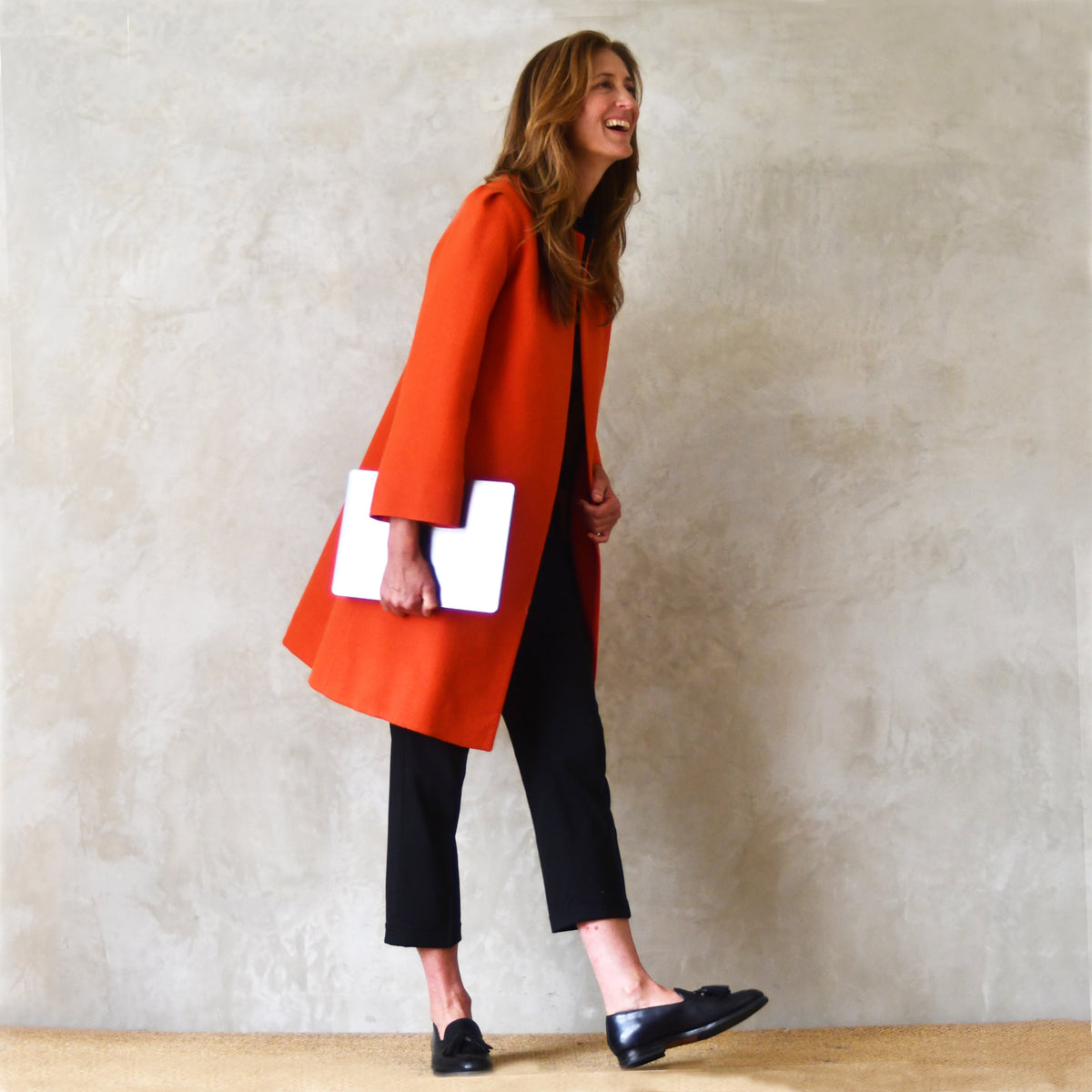 Bespoke Shoulder Detail Trapeze Coat in Burnt Orange Wool Crepe. An elegant alternative to a jacket, our mid length trapeze coat will take you to town, work, country and back. Handmade in Great Britain. Side on view.