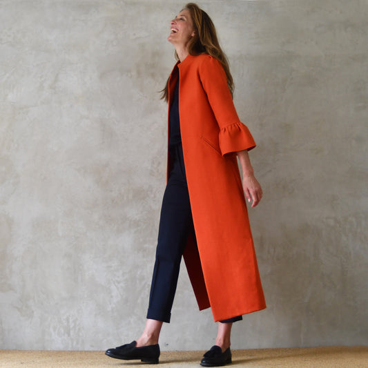 A-Line Bell Sleeve Coat in Orange Wool Crepe. This is an elegant longer length A-Line coat in a stupendous burnt orange wool crepe from Yorkshire. With a magnificent drape and delicate sleeve and shoulder detailing, this coat will take you everywhere. Entirely made in Great Britain. Side View.
