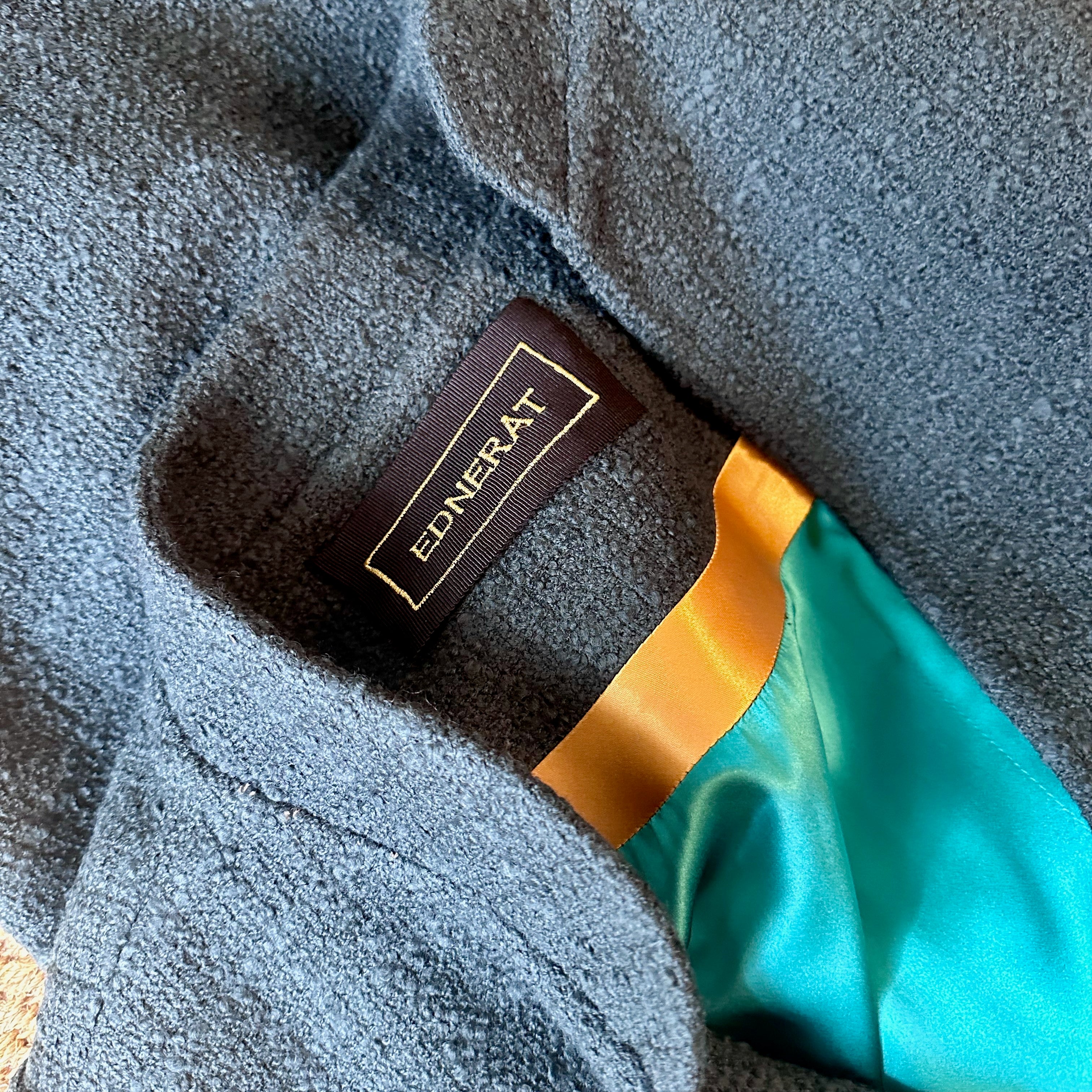 Bespoke A-Line Bell-Sleeve Coat in Bottle Green Linton Tweeds Boucle. A longer length A-line coat with frill cuff details in a warmer weight deep green wool bouclé. Hand cut, made and finished in London. Made in Britain. Inside collar view showing embroidered label, gold satin trim and matched green silk lining.