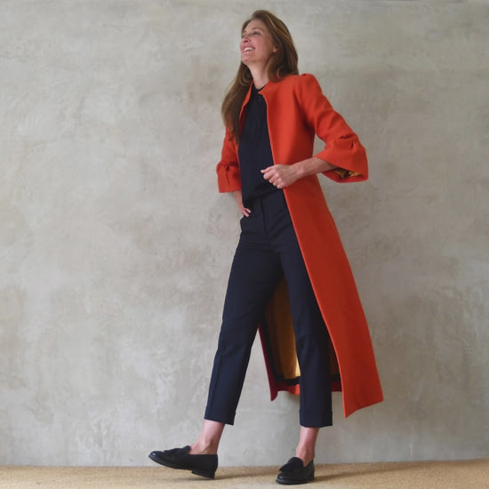Bespoke Bell Sleeve A-Line Coat in Orange Wool Crepe. This is an elegant longer length A-Line coat in a stupendous burnt orange wool crepe from Yorkshire. With a magnificent drape and delicate sleeve detailing, this coat will take you everywhere. Entirely made in Great Britain.